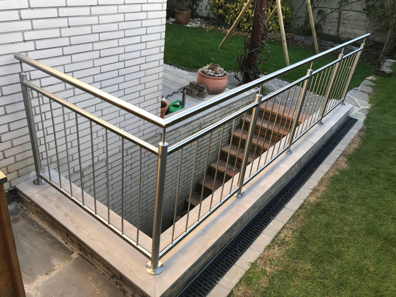 Edelstahl-Terrassengeländer mit Senkrechtstäben, um die Ecke über einen Kellerabgang geführt